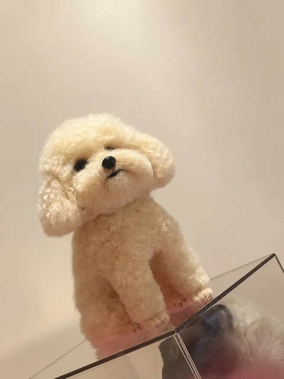 A cream needle-felted poodle standing on four legs, with a curly coat, dark eyes and a dark nose.