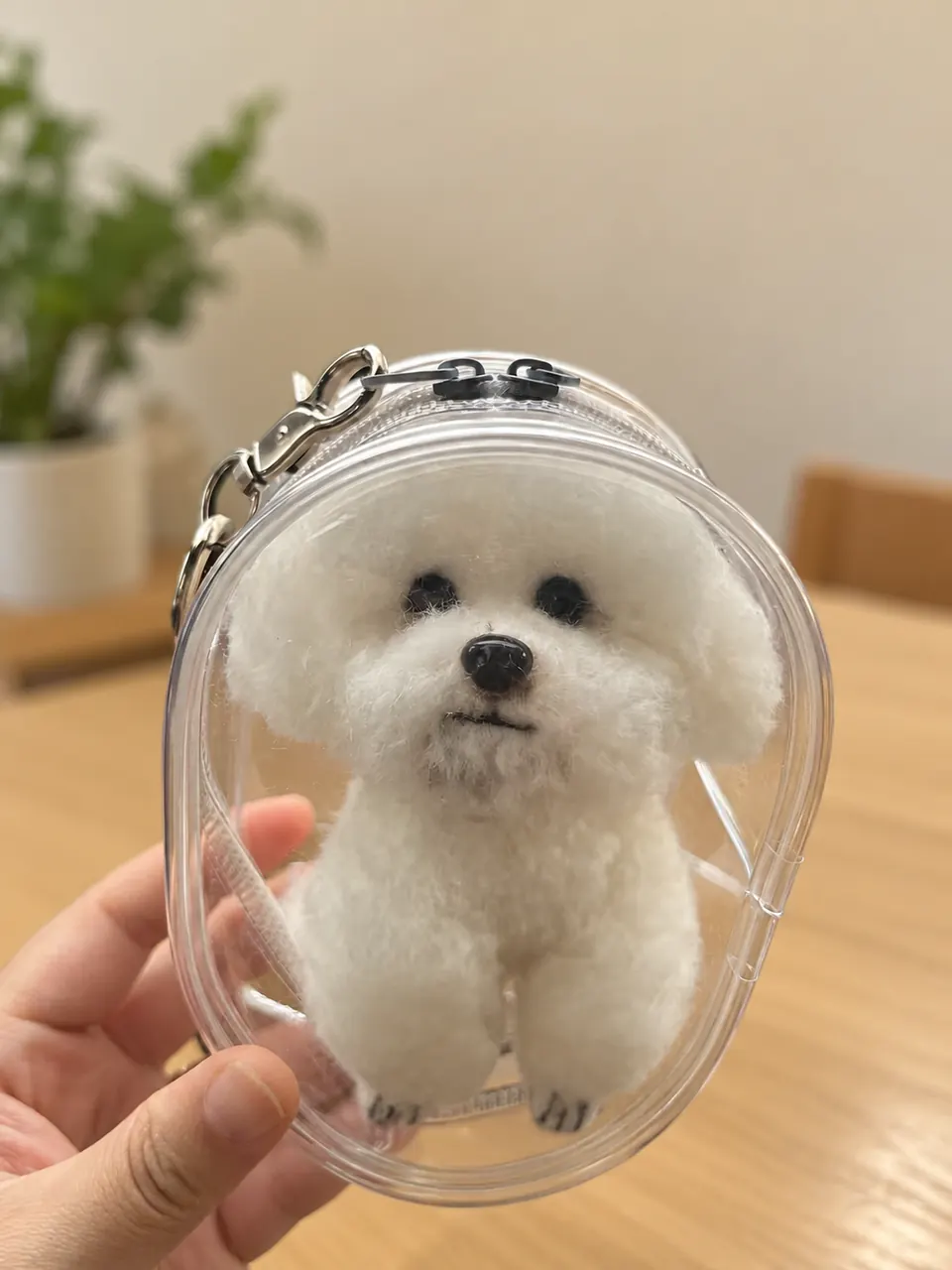 A needle-felted white dog inside a clear oval case on a keyring, held in one hand.